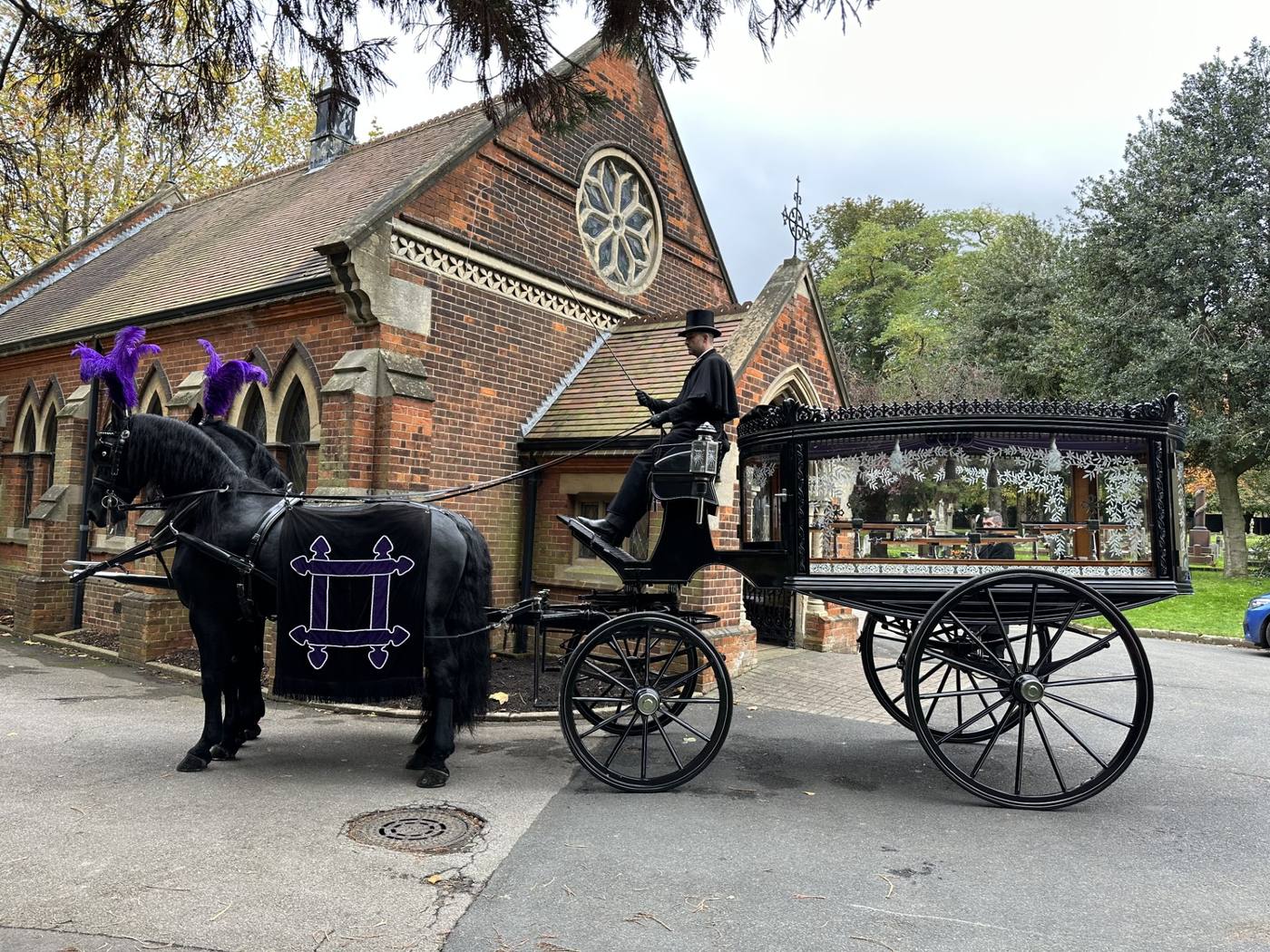 Black glass horse-drawn hearse drawn by black plumed horses